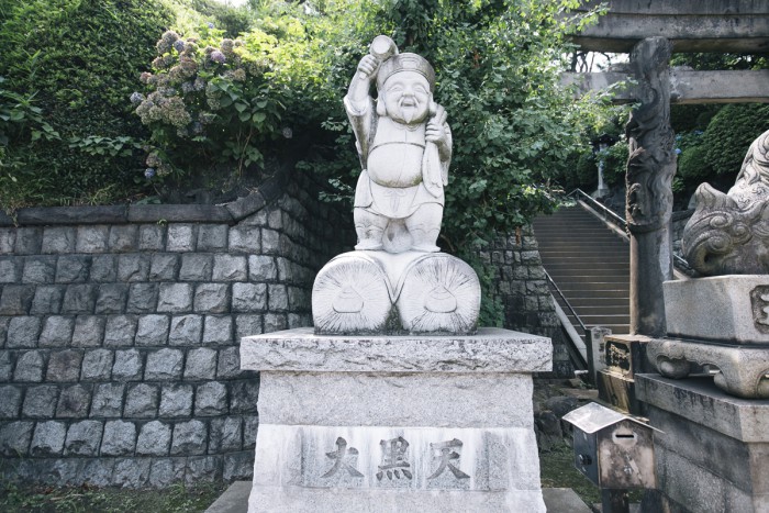 A stone statue of Daikokuten with a plump and happy-looking smile sitting beside the stone steps.